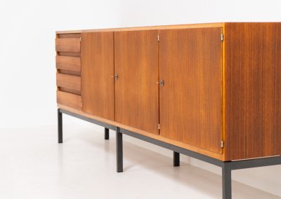 XL Modernist sideboard by Behr Möbel (Germany, 1950s). This striking modernist sideboard was produced in the 1950s by the renowned German manufacturer Behr Möbel, best known for the iconic B40 model. Expertly crafted from rich teak wood, the piece rests on a sleek metal base that adds to its architectural presence. It features four drawers and three doors, offering generous storage space with adjustable shelves inside. The sideboard is in very good condition, with fully functional locks.