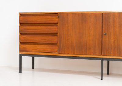 XL Modernist sideboard by Behr Möbel (Germany, 1950s). This striking modernist sideboard was produced in the 1950s by the renowned German manufacturer Behr Möbel, best known for the iconic B40 model. Expertly crafted from rich teak wood, the piece rests on a sleek metal base that adds to its architectural presence. It features four drawers and three doors, offering generous storage space with adjustable shelves inside. The sideboard is in very good condition, with fully functional locks.