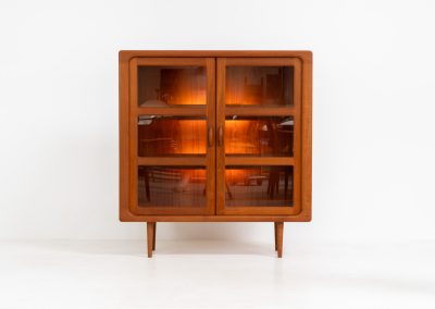 Stunning showcase by Svend Dyrlund (Denmark, 1960s). This exceptional piece features elegant doors with glass panels and beautifully crafted wooden handles, two adjustable shelves, and convenient backlights behind each shelf to highlight your displayed items. Made from rich teak with a natural woodgrain, it perfectly combines functionality with the timeless characteristic of Danish modern design. In splendid condition & labeled by maker.