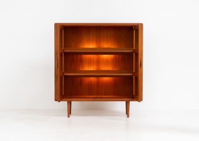 Stunning showcase by Svend Dyrlund (Denmark, 1960s). This exceptional piece features elegant doors with glass panels and beautifully crafted wooden handles, two adjustable shelves, and convenient backlights behind each shelf to highlight your displayed items. Made from rich teak with a natural woodgrain, it perfectly combines functionality with the timeless characteristic of Danish modern design. In splendid condition & labeled by maker.