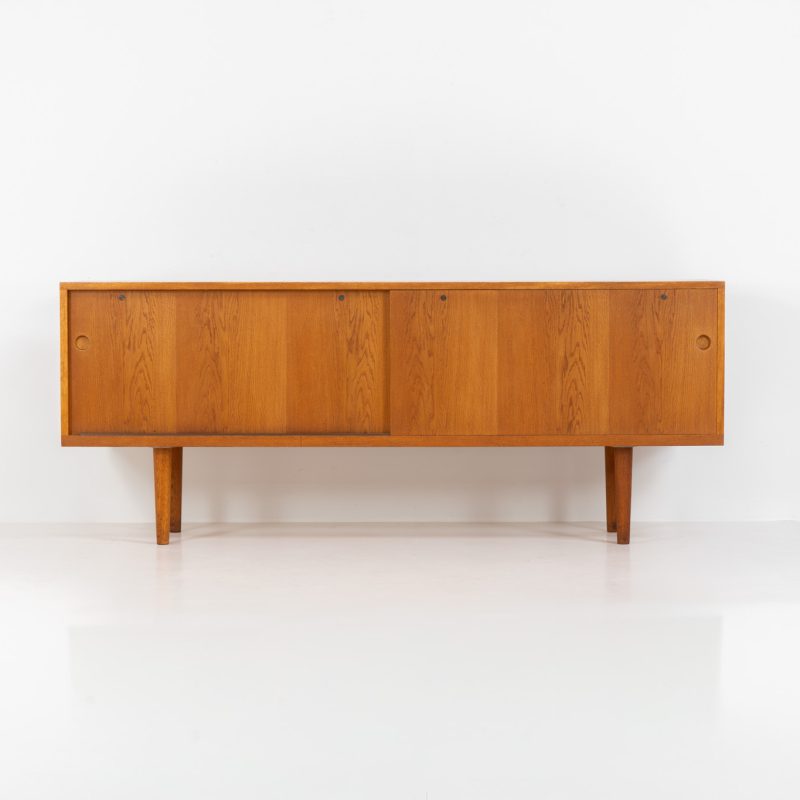 Rare and important RY26 sideboard by Hans J. Wegner for Ry Møbler (Denmark, 1950s). This incredible piece is composed of delicately grained oak with a stunning honey hued stain. It contains two large sliding doors with round inset handles, adjustable shelves and four modular drawers on the inside. This hard to find piece remains in very good vintage condition. It is designed by the the renowned Hans J. Wegner who won multiple awards and honors throughout his carreer.