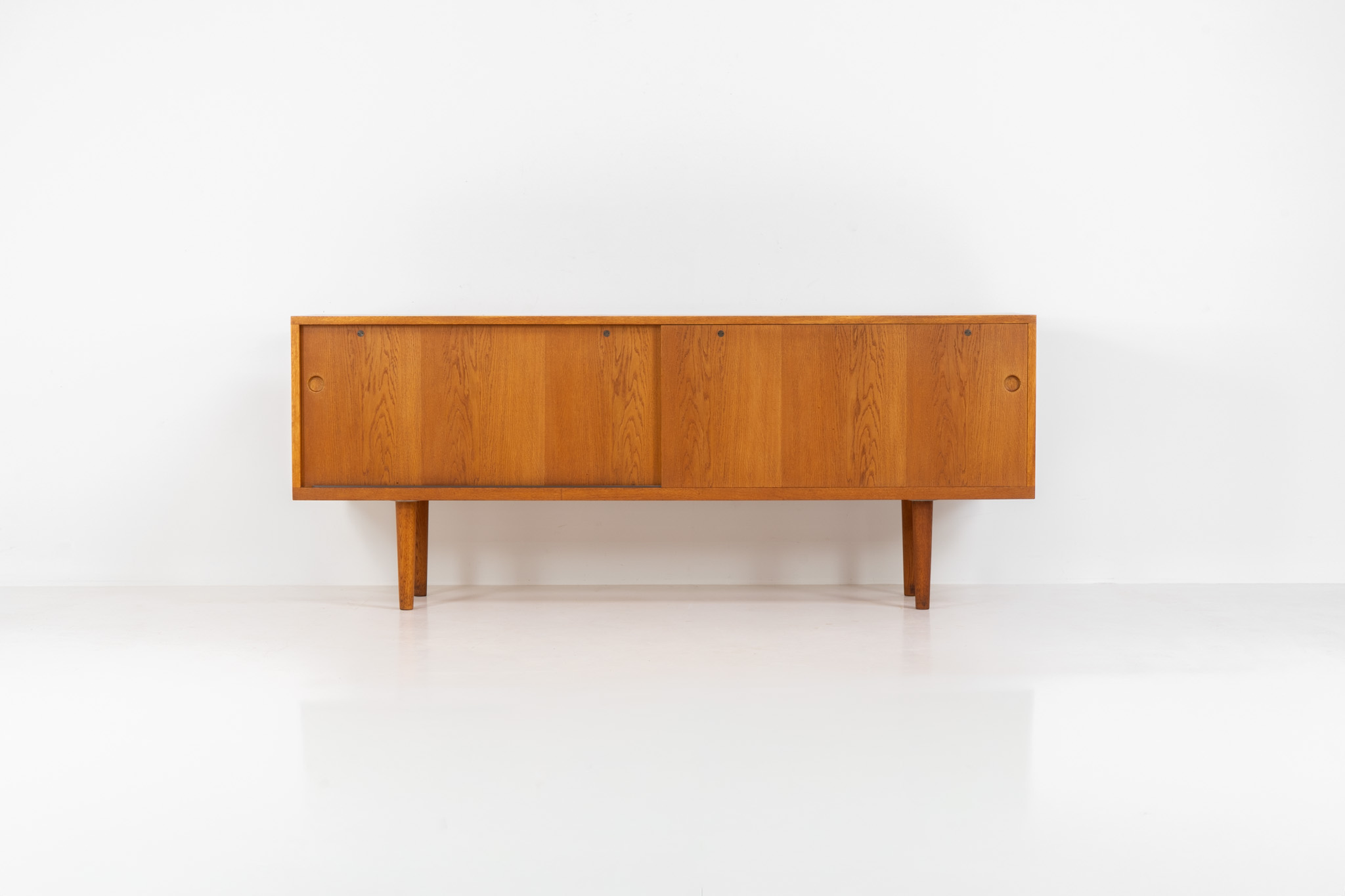 Rare and important RY26 sideboard by Hans J. Wegner for Ry Møbler (Denmark, 1950s). This incredible piece is composed of delicately grained oak with a stunning honey hued stain. It contains two large sliding doors with round inset handles, adjustable shelves and four modular drawers on the inside. This hard to find piece remains in very good vintage condition. It is designed by the the renowned Hans J. Wegner who won multiple awards and honors throughout his carreer.