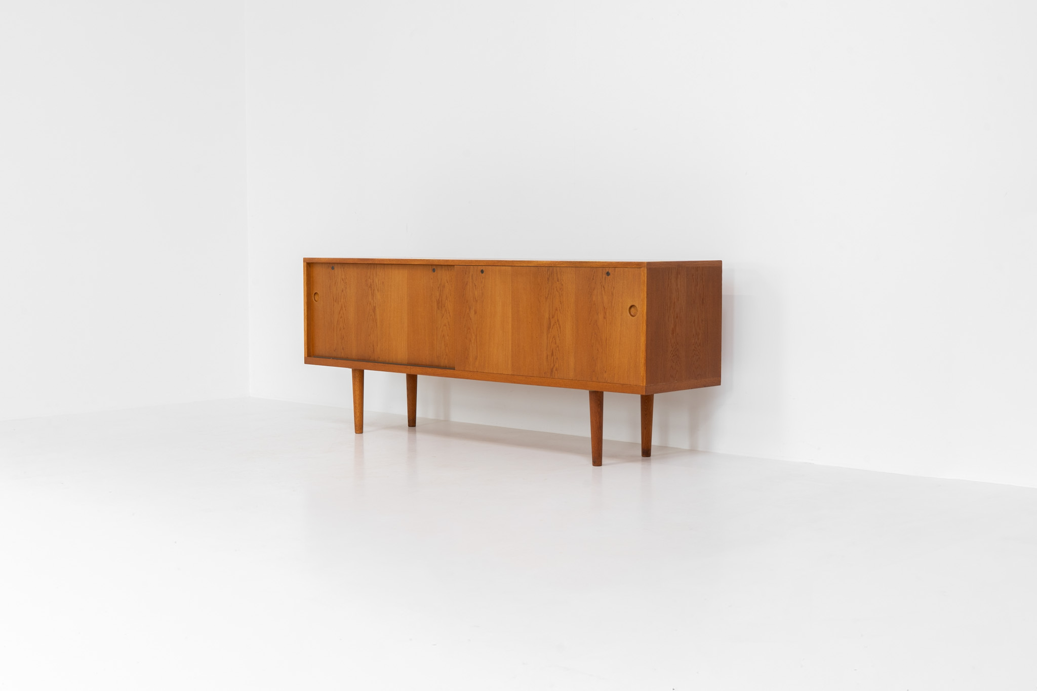Rare and important RY26 sideboard by Hans J. Wegner for Ry Møbler (Denmark, 1950s). This incredible piece is composed of delicately grained oak with a stunning honey hued stain. It contains two large sliding doors with round inset handles, adjustable shelves and four modular drawers on the inside. This hard to find piece remains in very good vintage condition. It is designed by the the renowned Hans J. Wegner who won multiple awards and honors throughout his carreer.