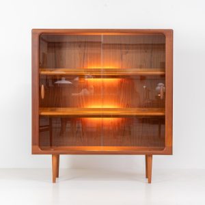 Stunning showcase by Svend Dyrlund (Denmark, 1960s). This exceptional piece features elegant glass doors with beautifully crafted wooden handles, two adjustable shelves, and convenient backlights behind each shelf to highlight your displayed items. Made from rich teak with a natural woodgrain, it perfectly combines functionality with the timeless characteristic of Danish modern design. In splendid condition.