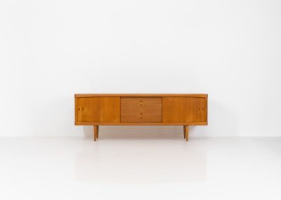 Exceptional sideboard by Henry W. Klein for Bramin in oak (Denmark, 1960s). This piece is a true masterpiece of Danish mid-century design. Crafted from high-quality materials, it showcases exquisite attention to detail, from the sculptural integrated handles to the beautifully crafted corner joints. The sideboard offers the perfect balance of aesthetics and functionality. It features two large sliding doors with adjustable shelves behind them and four drawers. The highboard is in very good condition and marked by maker.