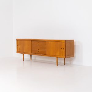 Exceptional sideboard by Henry W. Klein for Bramin in oak (Denmark, 1960s). This piece is a true masterpiece of Danish mid-century design. Crafted from high-quality materials, it showcases exquisite attention to detail, from the sculptural integrated handles to the beautifully crafted corner joints. The sideboard offers the perfect balance of aesthetics and functionality. It features two large sliding doors with adjustable shelves behind them and four drawers. The highboard is in very good condition and marked by maker.