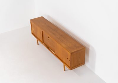 Exceptional sideboard by Henry W. Klein for Bramin in oak (Denmark, 1960s). This piece is a true masterpiece of Danish mid-century design. Crafted from high-quality materials, it showcases exquisite attention to detail, from the sculptural integrated handles to the beautifully crafted corner joints. The sideboard offers the perfect balance of aesthetics and functionality. It features two large sliding doors with adjustable shelves behind them and four drawers. The highboard is in very good condition and marked by maker.
