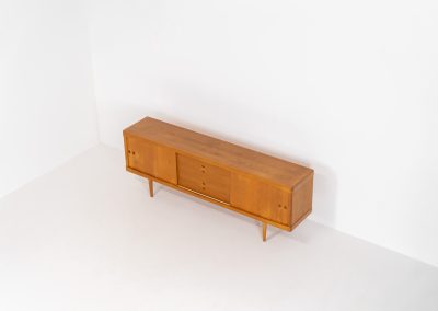 Exceptional sideboard by Henry W. Klein for Bramin in oak (Denmark, 1960s). This piece is a true masterpiece of Danish mid-century design. Crafted from high-quality materials, it showcases exquisite attention to detail, from the sculptural integrated handles to the beautifully crafted corner joints. The sideboard offers the perfect balance of aesthetics and functionality. It features two large sliding doors with adjustable shelves behind them and four drawers. The highboard is in very good condition and marked by maker.