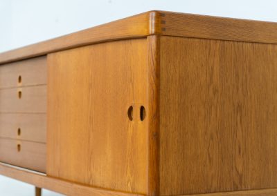 Exceptional sideboard by Henry W. Klein for Bramin in oak (Denmark, 1960s). This piece is a true masterpiece of Danish mid-century design. Crafted from high-quality materials, it showcases exquisite attention to detail, from the sculptural integrated handles to the beautifully crafted corner joints. The sideboard offers the perfect balance of aesthetics and functionality. It features two large sliding doors with adjustable shelves behind them and four drawers. The highboard is in very good condition and marked by maker.