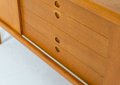 Exceptional sideboard by Henry W. Klein for Bramin in oak (Denmark, 1960s). This piece is a true masterpiece of Danish mid-century design. Crafted from high-quality materials, it showcases exquisite attention to detail, from the sculptural integrated handles to the beautifully crafted corner joints. The sideboard offers the perfect balance of aesthetics and functionality. It features two large sliding doors with adjustable shelves behind them and four drawers. The highboard is in very good condition and marked by maker.