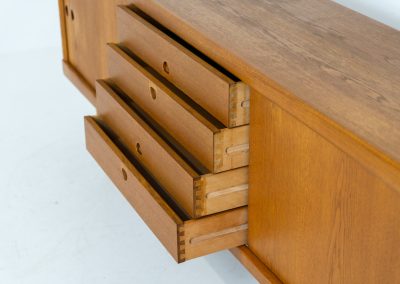 Exceptional sideboard by Henry W. Klein for Bramin in oak (Denmark, 1960s). This piece is a true masterpiece of Danish mid-century design. Crafted from high-quality materials, it showcases exquisite attention to detail, from the sculptural integrated handles to the beautifully crafted corner joints. The sideboard offers the perfect balance of aesthetics and functionality. It features two large sliding doors with adjustable shelves behind them and four drawers. The highboard is in very good condition and marked by maker.