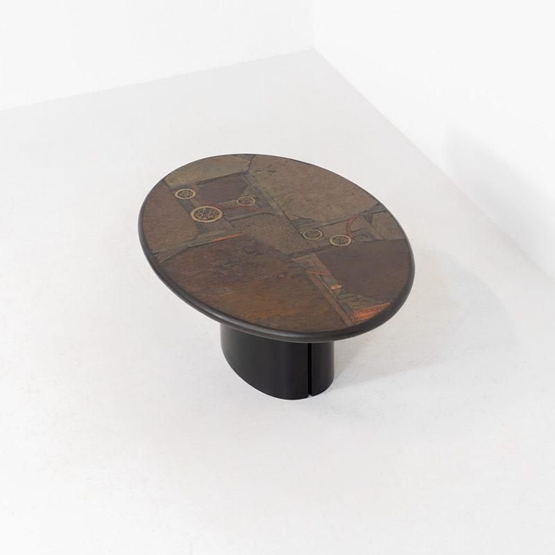 Brutalist coffee table by C. Kneip (Germany, 1990s). A powerful and sculptural brutalist coffee table by German designer C. Kneip, dating from the 1990s. The design is defined by its expressive materiality and architectural presence. The substantial tabletop is crafted from Indian slate and enriched with inlaid elements of lava stone, copper, and brass. These materials are arranged in a richly textured, almost relief-like composition, creating a striking interplay of color, surface, and depth. The heavy stone top is supported by a black lacquered wooden base, providing a sense of grounded solidity. The table is marked by the maker and retains its original certificate. Presented in splendid condition.