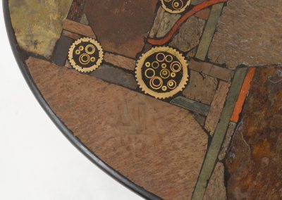 Brutalist coffee table by C. Kneip (Germany, 1990s). A powerful and sculptural brutalist coffee table by German designer C. Kneip, dating from the 1990s. The design is defined by its expressive materiality and architectural presence. The substantial tabletop is crafted from Indian slate and enriched with inlaid elements of lava stone, copper, and brass. These materials are arranged in a richly textured, almost relief-like composition, creating a striking interplay of color, surface, and depth. The heavy stone top is supported by a black lacquered wooden base, providing a sense of grounded solidity. The table is marked by the maker and retains its original certificate. Presented in splendid condition.