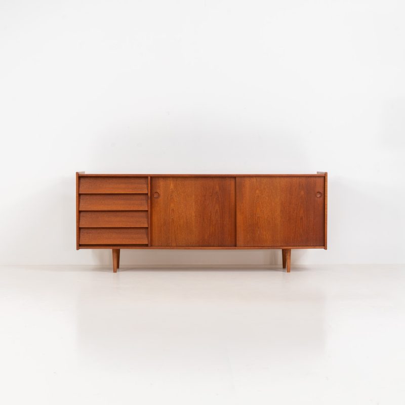 Teak sideboard by Nils Jonsson for Hugo Troeds (Sweden, 1950s). Elegant sideboard by Swedish designer Nils Jonsson, executed in warm teak. The clean, architectural form is complemented by tapered legs and balanced proportions. A distinctive feature of this piece is the set of sculpted, stepped drawers, offering both visual rhythm and practical storage. Sliding doors reveal generous interior space, making the sideboard as functional as it is refined. A timeless example of Scandinavian modern design, presented in excellent vintage condition.