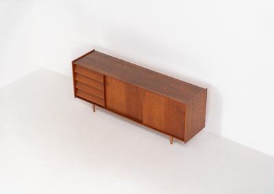 Teak sideboard by Nils Jonsson for Hugo Troeds (Sweden, 1950s). Elegant sideboard by Swedish designer Nils Jonsson, executed in warm teak. The clean, architectural form is complemented by tapered legs and balanced proportions. A distinctive feature of this piece is the set of sculpted, stepped drawers, offering both visual rhythm and practical storage. Sliding doors reveal generous interior space, making the sideboard as functional as it is refined. A timeless example of Scandinavian modern design, presented in excellent vintage condition.