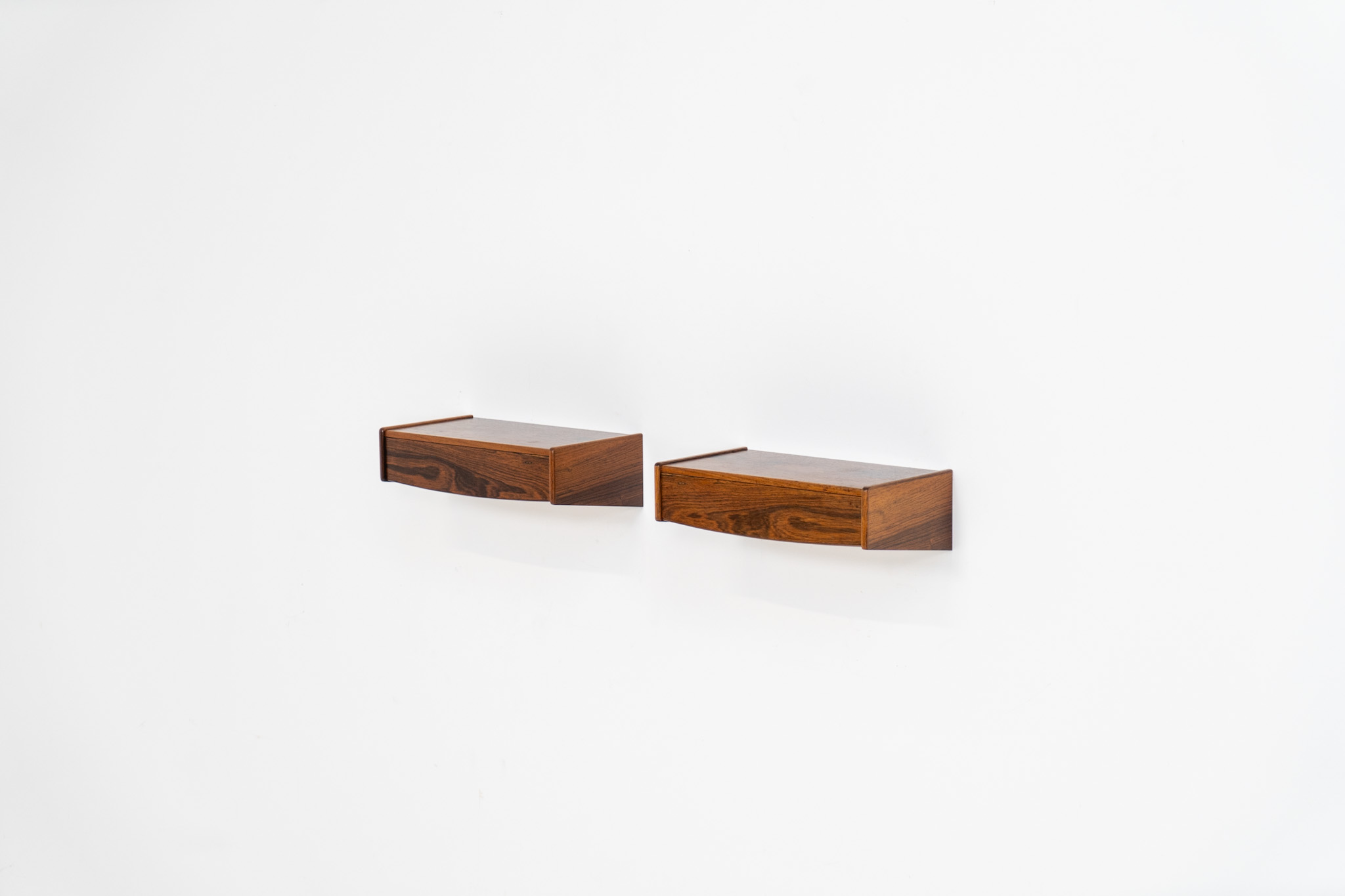 Pair of floating bedside tables in rosewood (Denmark, 1960s). This beautiful pair of bedside tables is easily mounted to the wall and contains a small drawer. They offer a minimalist appearance and a beautiful woodgrain. In very good condition with minimal traces of use visible.