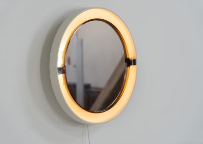 Model A41 backlit wall mirror by Allibert (Germany, 1970s). A striking space age design by Allibert, Germany. This Model A41 mirror is crafted from molded plastic and designed to hold four E14 bulbs inside, operated by a pull switch on the side. When illuminated, the translucent plastic frame softly diffuses the light, creating a warm halo effect around the mirror glass. The mirror can be tilted up or down, adding both functionality and a sculptural presence to the piece. Presented in good vintage condition with light, age-appropriate wear.