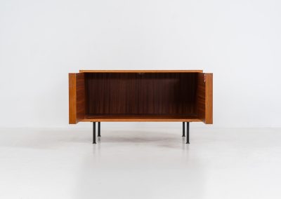Minimalist cabinet by Gunter Renkel for Rego (Germany, 1960s). Crafted in warm teak, the cabinet features clean architectural lines, two doors, and a beautifully balanced composition. The slender black metal legs create a subtle contrast and give the piece a light, elevated appearance. Compact yet versatile, it works perfectly as a low sideboard, media cabinet, or storage unit in both modern and mid-century interiors. Its in very good vintage condition. Make sure to check out the dimensions as it’s slightly deeper than your average cabinet.