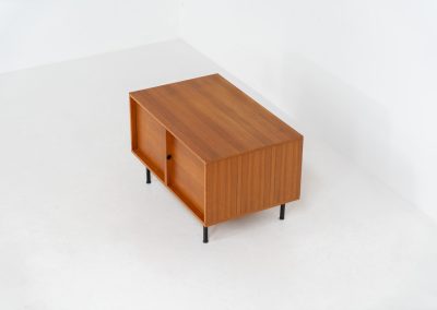 Minimalist cabinet by Gunter Renkel for Rego (Germany, 1960s). Crafted in warm teak, the cabinet features clean architectural lines, two doors, and a beautifully balanced composition. The slender black metal legs create a subtle contrast and give the piece a light, elevated appearance. Compact yet versatile, it works perfectly as a low sideboard, media cabinet, or storage unit in both modern and mid-century interiors. Its in very good vintage condition. Make sure to check out the dimensions as it’s slightly deeper than your average cabinet.