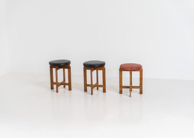 Very rare set of stools by Uno & Östen Kristiansson for Luxus Vittsjö (Sweden, 1950s). A highly collectible find, designed by the renowned brothers Uno & Östen Kristiansson and a true masterclass in Scandinavian architectural furniture. They consist of a solid oak cross-shaped base and a round leather seat, two in black and one in red. They are in used vintage condition with a nice patina on the seats and visible using traces on the wood. The two black stools can be sold separately upon request.