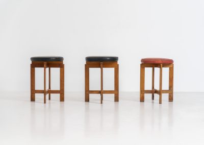Very rare set of stools by Uno & Östen Kristiansson for Luxus Vittsjö (Sweden, 1950s). A highly collectible find, designed by the renowned brothers Uno & Östen Kristiansson and a true masterclass in Scandinavian architectural furniture. They consist of a solid oak cross-shaped base and a round leather seat, two in black and one in red. They are in used vintage condition with a nice patina on the seats and visible using traces on the wood. The two black stools can be sold separately upon request.