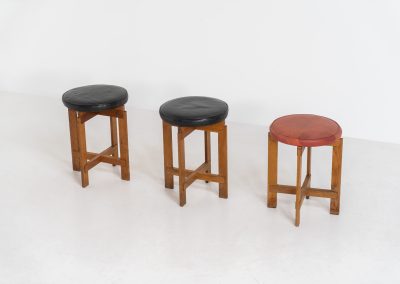 Very rare set of stools by Uno & Östen Kristiansson for Luxus Vittsjö (Sweden, 1950s). A highly collectible find, designed by the renowned brothers Uno & Östen Kristiansson and a true masterclass in Scandinavian architectural furniture. They consist of a solid oak cross-shaped base and a round leather seat, two in black and one in red. They are in used vintage condition with a nice patina on the seats and visible using traces on the wood. The two black stools can be sold separately upon request.