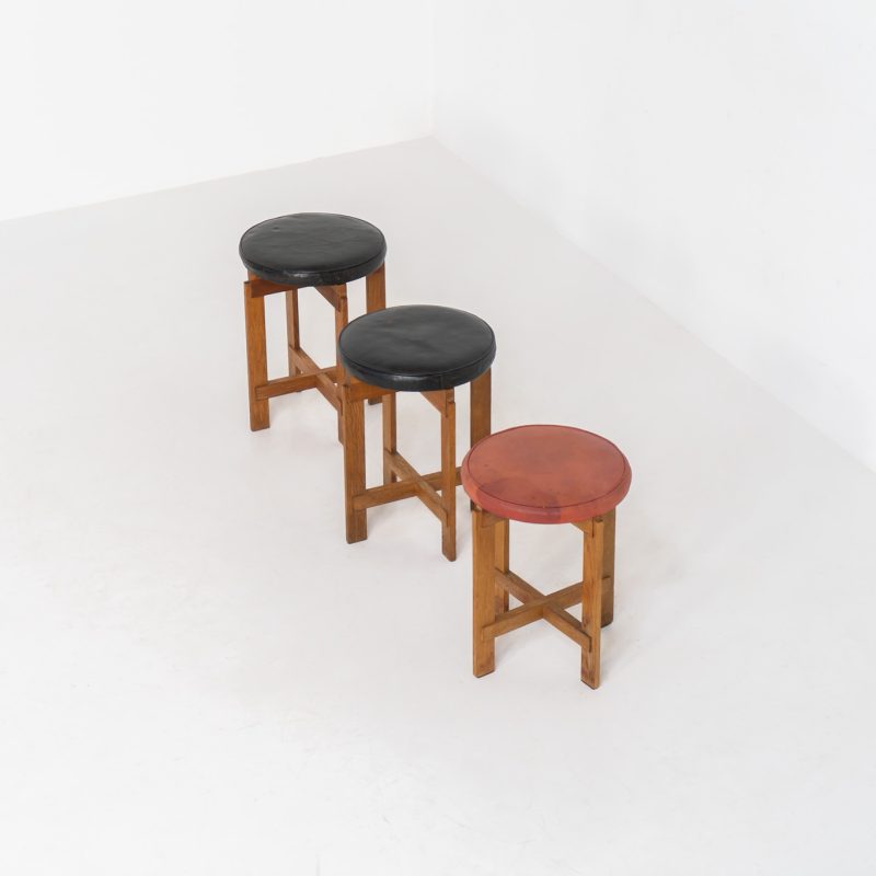 Very rare set of stools by Uno & Östen Kristiansson for Luxus Vittsjö (Sweden, 1950s). A highly collectible find, designed by the renowned brothers Uno & Östen Kristiansson and a true masterclass in Scandinavian architectural furniture. They consist of a solid oak cross-shaped base and a round leather seat, two in black and one in red. They are in used vintage condition with a nice patina on the seats and visible using traces on the wood. The two black stools can be sold separately upon request.