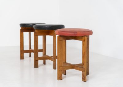 Very rare set of stools by Uno & Östen Kristiansson for Luxus Vittsjö (Sweden, 1950s). A highly collectible find, designed by the renowned brothers Uno & Östen Kristiansson and a true masterclass in Scandinavian architectural furniture. They consist of a solid oak cross-shaped base and a round leather seat, two in black and one in red. They are in used vintage condition with a nice patina on the seats and visible using traces on the wood. The two black stools can be sold separately upon request.