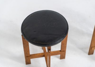 Very rare set of stools by Uno & Östen Kristiansson for Luxus Vittsjö (Sweden, 1950s). A highly collectible find, designed by the renowned brothers Uno & Östen Kristiansson and a true masterclass in Scandinavian architectural furniture. They consist of a solid oak cross-shaped base and a round leather seat, two in black and one in red. They are in used vintage condition with a nice patina on the seats and visible using traces on the wood. The two black stools can be sold separately upon request.