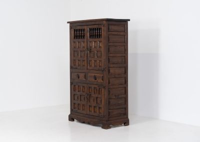Stunning Spanish brutalist cabinet, 1950s. Striking and architectural, this 1950s Spanish cabinet is a powerful example of brutalist craftsmanship. Executed in solid wood, it features a deeply carved geometric façade with repetitive panel motifs that create a strong sense of rhythm and depth. The upper doors are accented with turned spindle details, adding contrast to the otherwise bold and graphic design. Original iron hardware, including hinges and latches, reinforces its rustic character. Behind the doors, the cabinet offers generous storage, making it as functional as it is sculptural. The warm patina of the wood enhances its presence, giving it a timeless, almost monolithic feel.