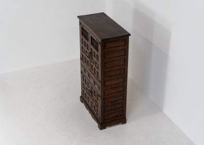 Stunning Spanish brutalist cabinet, 1950s. Striking and architectural, this 1950s Spanish cabinet is a powerful example of brutalist craftsmanship. Executed in solid wood, it features a deeply carved geometric façade with repetitive panel motifs that create a strong sense of rhythm and depth. The upper doors are accented with turned spindle details, adding contrast to the otherwise bold and graphic design. Original iron hardware, including hinges and latches, reinforces its rustic character. Behind the doors, the cabinet offers generous storage, making it as functional as it is sculptural. The warm patina of the wood enhances its presence, giving it a timeless, almost monolithic feel.
