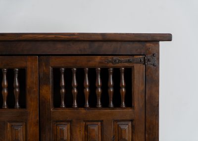 Stunning Spanish brutalist cabinet, 1950s. Striking and architectural, this 1950s Spanish cabinet is a powerful example of brutalist craftsmanship. Executed in solid wood, it features a deeply carved geometric façade with repetitive panel motifs that create a strong sense of rhythm and depth. The upper doors are accented with turned spindle details, adding contrast to the otherwise bold and graphic design. Original iron hardware, including hinges and latches, reinforces its rustic character. Behind the doors, the cabinet offers generous storage, making it as functional as it is sculptural. The warm patina of the wood enhances its presence, giving it a timeless, almost monolithic feel.