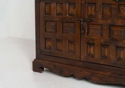 Stunning Spanish brutalist cabinet, 1950s. Striking and architectural, this 1950s Spanish cabinet is a powerful example of brutalist craftsmanship. Executed in solid wood, it features a deeply carved geometric façade with repetitive panel motifs that create a strong sense of rhythm and depth. The upper doors are accented with turned spindle details, adding contrast to the otherwise bold and graphic design. Original iron hardware, including hinges and latches, reinforces its rustic character. Behind the doors, the cabinet offers generous storage, making it as functional as it is sculptural. The warm patina of the wood enhances its presence, giving it a timeless, almost monolithic feel.