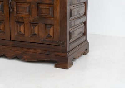 Stunning Spanish brutalist cabinet, 1950s. Striking and architectural, this 1950s Spanish cabinet is a powerful example of brutalist craftsmanship. Executed in solid wood, it features a deeply carved geometric façade with repetitive panel motifs that create a strong sense of rhythm and depth. The upper doors are accented with turned spindle details, adding contrast to the otherwise bold and graphic design. Original iron hardware, including hinges and latches, reinforces its rustic character. Behind the doors, the cabinet offers generous storage, making it as functional as it is sculptural. The warm patina of the wood enhances its presence, giving it a timeless, almost monolithic feel.