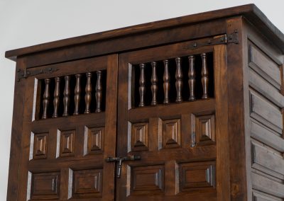 Stunning Spanish brutalist cabinet, 1950s. Striking and architectural, this 1950s Spanish cabinet is a powerful example of brutalist craftsmanship. Executed in solid wood, it features a deeply carved geometric façade with repetitive panel motifs that create a strong sense of rhythm and depth. The upper doors are accented with turned spindle details, adding contrast to the otherwise bold and graphic design. Original iron hardware, including hinges and latches, reinforces its rustic character. Behind the doors, the cabinet offers generous storage, making it as functional as it is sculptural. The warm patina of the wood enhances its presence, giving it a timeless, almost monolithic feel.