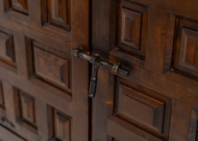 Stunning Spanish brutalist cabinet, 1950s. Striking and architectural, this 1950s Spanish cabinet is a powerful example of brutalist craftsmanship. Executed in solid wood, it features a deeply carved geometric façade with repetitive panel motifs that create a strong sense of rhythm and depth. The upper doors are accented with turned spindle details, adding contrast to the otherwise bold and graphic design. Original iron hardware, including hinges and latches, reinforces its rustic character. Behind the doors, the cabinet offers generous storage, making it as functional as it is sculptural. The warm patina of the wood enhances its presence, giving it a timeless, almost monolithic feel.