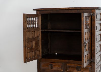 Stunning Spanish brutalist cabinet, 1950s. Striking and architectural, this 1950s Spanish cabinet is a powerful example of brutalist craftsmanship. Executed in solid wood, it features a deeply carved geometric façade with repetitive panel motifs that create a strong sense of rhythm and depth. The upper doors are accented with turned spindle details, adding contrast to the otherwise bold and graphic design. Original iron hardware, including hinges and latches, reinforces its rustic character. Behind the doors, the cabinet offers generous storage, making it as functional as it is sculptural. The warm patina of the wood enhances its presence, giving it a timeless, almost monolithic feel.