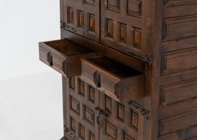 Stunning Spanish brutalist cabinet, 1950s. Striking and architectural, this 1950s Spanish cabinet is a powerful example of brutalist craftsmanship. Executed in solid wood, it features a deeply carved geometric façade with repetitive panel motifs that create a strong sense of rhythm and depth. The upper doors are accented with turned spindle details, adding contrast to the otherwise bold and graphic design. Original iron hardware, including hinges and latches, reinforces its rustic character. Behind the doors, the cabinet offers generous storage, making it as functional as it is sculptural. The warm patina of the wood enhances its presence, giving it a timeless, almost monolithic feel.