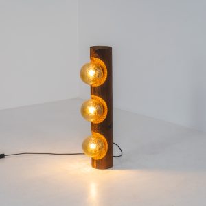 Sculptural floor lamp by Temde Leuchten (Switzerland, 1970s). This exceptional piece combines an organic form with a subtle brutalist character. It is crafted from solid burnt oak and features three round glass light sources that create a warm, atmospheric glow. Versatile in use, the lamp can function as a mid-height floor lamp, a table lamp, or even a wall-mounted piece thanks to its integrated rear mountings. The lamp remains in very good condition, with the wood showing a beautifully aged patina that enhances its character.
