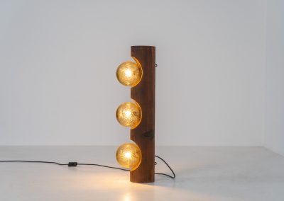 Sculptural floor lamp by Temde Leuchten (Switzerland, 1970s). This exceptional piece combines an organic form with a subtle brutalist character. It is crafted from solid burnt oak and features three round glass light sources that create a warm, atmospheric glow. Versatile in use, the lamp can function as a mid-height floor lamp, a table lamp, or even a wall-mounted piece thanks to its integrated rear mountings. The lamp remains in very good condition, with the wood showing a beautifully aged patina that enhances its character.