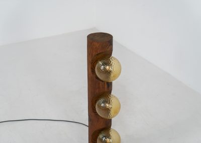 Sculptural floor lamp by Temde Leuchten (Switzerland, 1970s). This exceptional piece combines an organic form with a subtle brutalist character. It is crafted from solid burnt oak and features three round glass light sources that create a warm, atmospheric glow. Versatile in use, the lamp can function as a mid-height floor lamp, a table lamp, or even a wall-mounted piece thanks to its integrated rear mountings. The lamp remains in very good condition, with the wood showing a beautifully aged patina that enhances its character.
