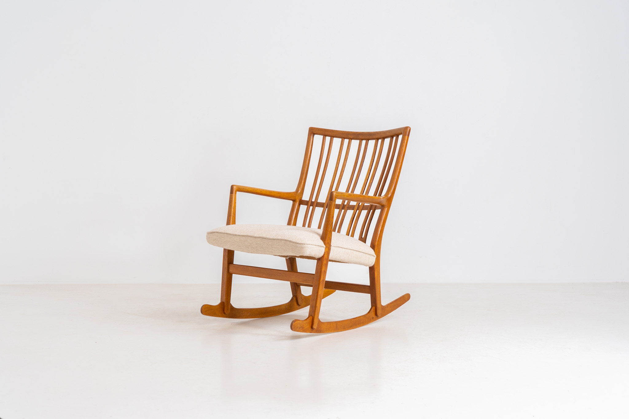 A rare “ML33” rocking chair by Hans J. Wegner for A. Mikael Laursen (Denmark, 1950s). Pure Danish craftsmanship from the 1950s, featuring a highly sculptural silhouette crafted from solid oak. A true masterpiece of mid-century design. The chair has been reupholstered in a beautifully textured of-white fabric and contains new straps.