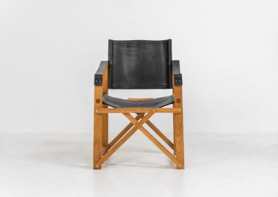 Oak & leather safari chair (Denmark, 1980s) A striking armchair from the 1980s, crafted from solid oak and fitted with a black leather seat and backrest. The design features a sturdy, architectural frame with visible joinery and cross-bracing, giving it a strong yet refined presence. It is easily foldable, reducing its footprint by roughly half when stored. The chair is in good condition, showing light signs of use and a beautiful natural patina on the leather.