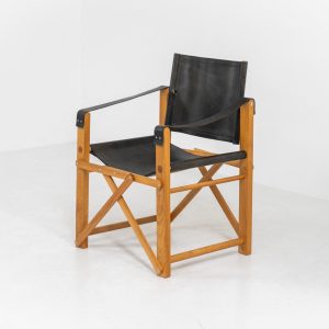 Oak & leather safari chair (Denmark, 1980s) A striking armchair from the 1980s, crafted from solid oak and fitted with a black leather seat and backrest. The design features a sturdy, architectural frame with visible joinery and cross-bracing, giving it a strong yet refined presence. It is easily foldable, reducing its footprint by roughly half when stored. The chair is in good condition, showing light signs of use and a beautiful natural patina on the leather.