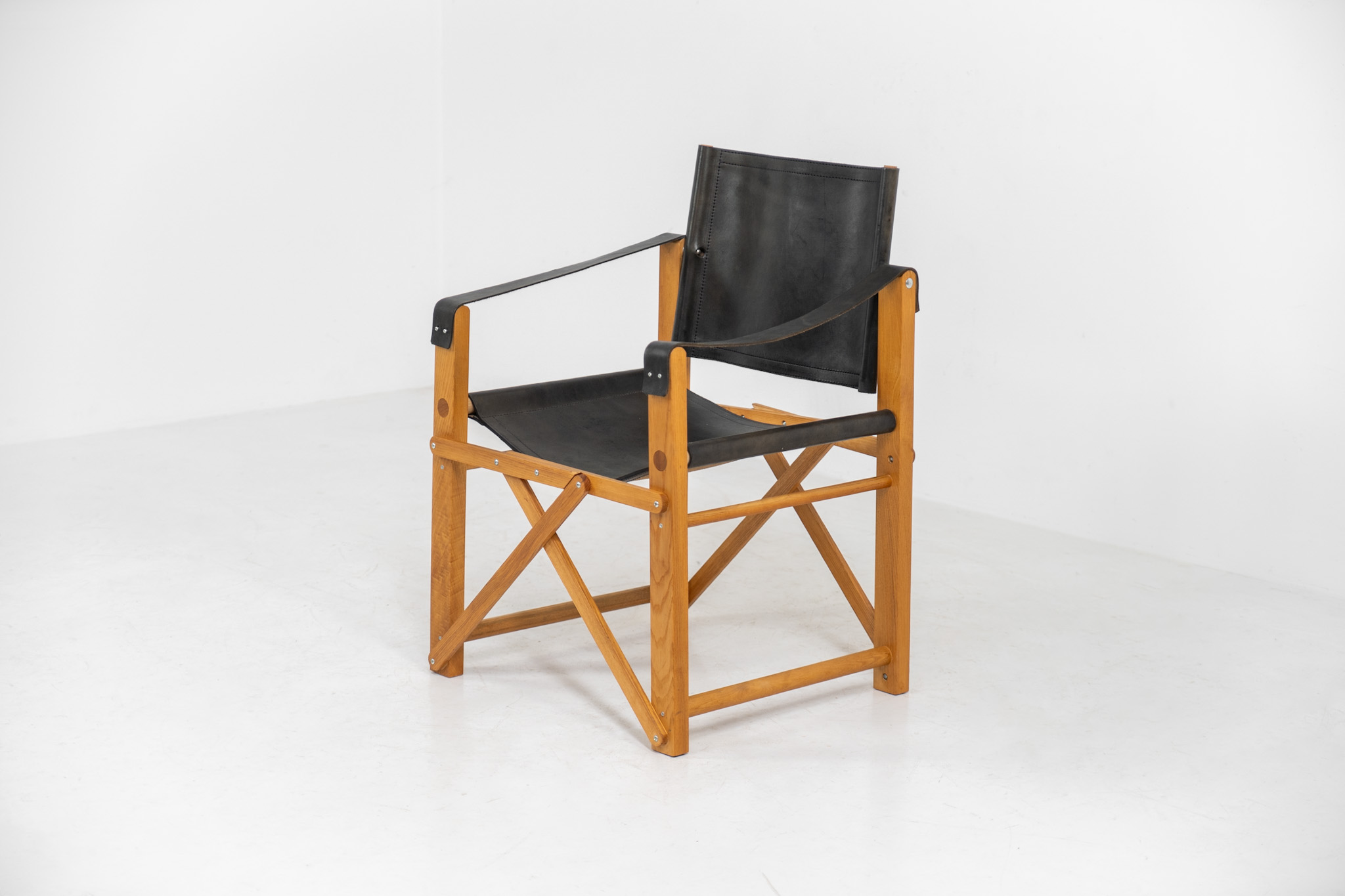 Oak & leather safari chair (Denmark, 1980s) A striking armchair from the 1980s, crafted from solid oak and fitted with a black leather seat and backrest. The design features a sturdy, architectural frame with visible joinery and cross-bracing, giving it a strong yet refined presence. It is easily foldable, reducing its footprint by roughly half when stored. The chair is in good condition, showing light signs of use and a beautiful natural patina on the leather.