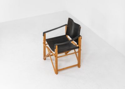 Oak & leather safari chair (Denmark, 1980s) A striking armchair from the 1980s, crafted from solid oak and fitted with a black leather seat and backrest. The design features a sturdy, architectural frame with visible joinery and cross-bracing, giving it a strong yet refined presence. It is easily foldable, reducing its footprint by roughly half when stored. The chair is in good condition, showing light signs of use and a beautiful natural patina on the leather.
