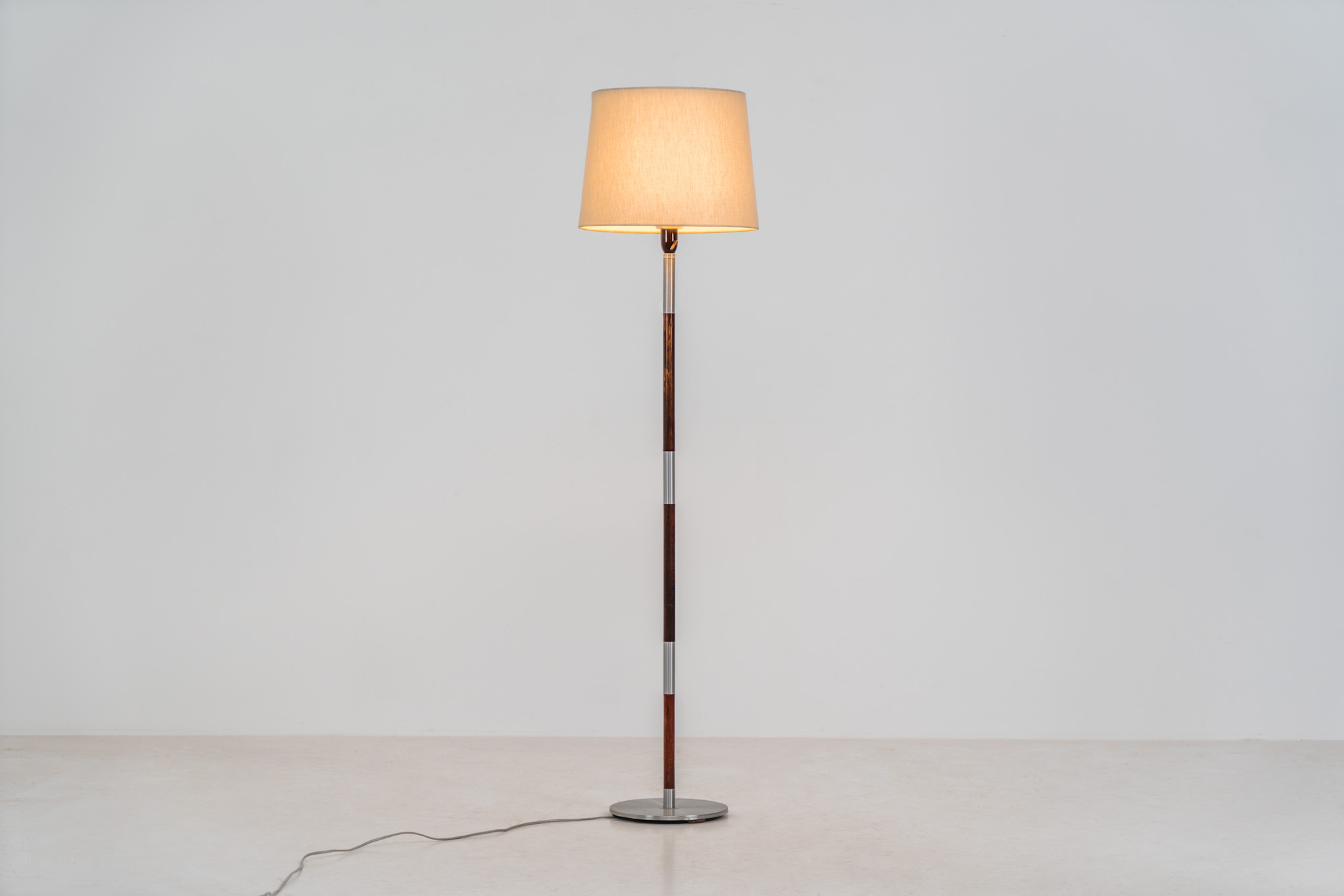 Rosewood & aluminium floorlamp attributed to Jo Hammerborg for Fog & Mørup (Denmark, 1960s). This elegant floor lamp features a sleek, minimalistic design, beautifully combining warm rosewood with refined aluminium details. While the model is often attributed to Jo Hammerborg, no official documentation has been found to fully confirm this. Regardless, it remains a striking example of high-quality Danish mid-century lighting. Presented in good condition, with normal age-related signs of use.