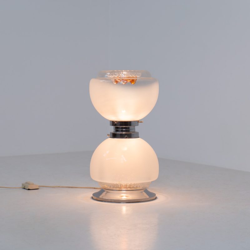Floor lamp by Toni Zuccheri for Mazzega (Italy, 1970s). 1970s floor lamp by Toni Zuccheri for Mazzega, combining sculptural opaline Murano glass with refined chrome details. The design is highlighted by subtle amber, drip-like inclusions, an iconic Zuccheri signature. When lit, it casts a warm, atmospheric glow that enhances the soft translucency of the glass, making it both a functional light source and a collectible piece of Italian design. The lamp can be used as a floor lamp, or a large table lamp. Splendid condition.