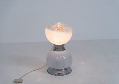 Floor lamp by Toni Zuccheri for Mazzega (Italy, 1970s). 1970s floor lamp by Toni Zuccheri for Mazzega, combining sculptural opaline Murano glass with refined chrome details. The design is highlighted by subtle amber, drip-like inclusions, an iconic Zuccheri signature. When lit, it casts a warm, atmospheric glow that enhances the soft translucency of the glass, making it both a functional light source and a collectible piece of Italian design. The lamp can be used as a floor lamp, or a large table lamp. Splendid condition.