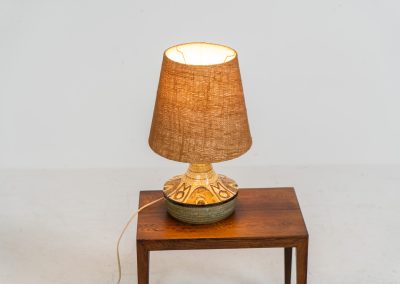 Ceramic table lamp by Søholm for Bornholmsk (Denmark, 1960s). This lamp offers a refined blend of beautiful textures and timeless design. It has handcrafted ceramic base with earthy colors, complimented by a raffia shade. The lamp is marked and remains in splendid condition.